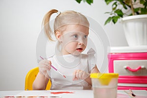 A Little Girl, With Tails On Her Head, Draws Watercolors Sitting At a Table. The Child Likes To Be Creative