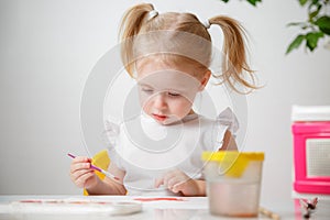 A Little Girl, With Tails On Her Head, Draws Watercolors Sitting At a Table. The Child Likes To Be Creative.