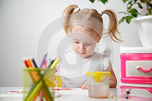 A Little Girl, With Tails On Her Head, Draws Watercolors Sitting At a Table. The Child Likes To Be Creative