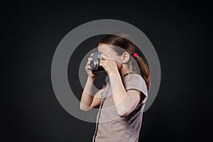 Little girl take photo with vintage camera at black background