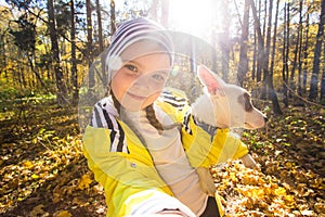 Little girl taking selfie with her dog at autumn park. Child posing with jack russell terrier for a picture on the