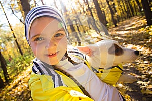 Little girl taking selfie with her dog at autumn park. Child posing with jack russell terrier for a picture on the