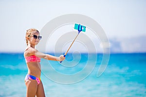 Little girl taking selfportrait by her smartphone on the beach. Kid enjoying her suumer vacation and making photos for