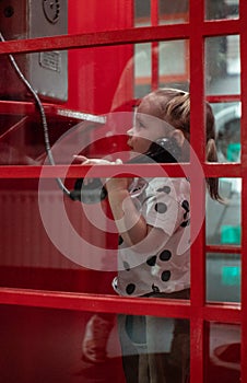 The little girl is talking on the phone in a red telephone booth Child girl neatly holds in her hand the receiver in a