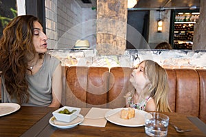 Little girl talking to mother sitting in restaurant