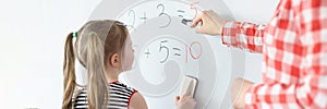 Little girl and teacher solving math equations on blackboard