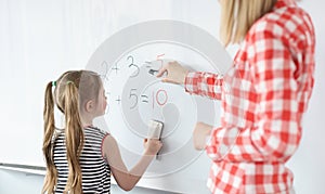 Little girl and teacher solving math equations on blackboard