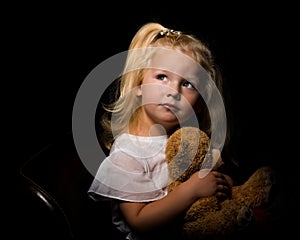 Little girl with a teddy bear on a black background.