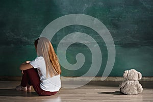 Little girl with teddy bear sitting on floor in empty room. Autism concept