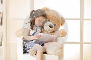 Little girl with Teddy bear watching her tablet computer