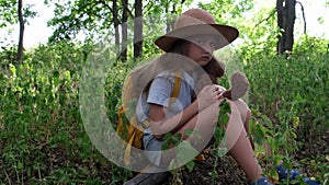 Little girl with a teddy bear and yellow backpack sits alone in the forest. Child tourist lost in the thicket. Upset kid