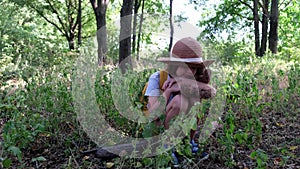 Little girl with a teddy bear and yellow backpack sits alone in the thicket. Child tourist lost in the forest. Upset