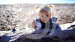 Little girl with teddy bears leans on a snag on the beach and nods her head