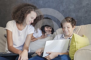 Little girl, teen boy and curly hair girl wirh laptop on sofa a