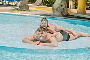 Little girl and teenage boy having fun in garden swimming pool on sunny warm day