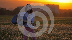 Little girl teenager sunglasses during sunset, dancing and playing guitar standing in a field near the house. concept celebration