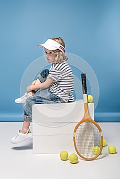 Little girl with tennis raquet and balls sitting on white boxes