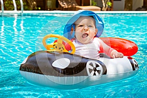 A little girl less than one year old is driving an inflatable boat car. She is screaming in the pool