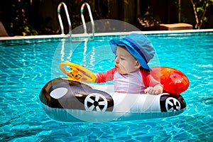 A little girl less than one year old is driving an inflatable boat in the shape of a car. She is surprised to touch the steering