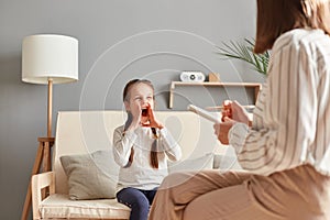Little girl at therapy session with psychologist expressing her emotions and frustrations by shouting loudly while specialist photo