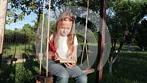 Little girl thinking and writing on nest swing