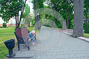 Little girl with thoughtful look sitting on bench in city park and thinking