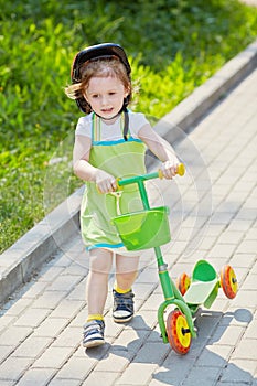 Little girl with three-wheeled scooter goes along