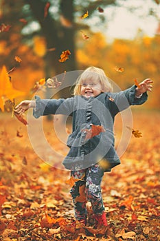 Little girl throwing yellow autumn leaves in the air in the park; autumn background