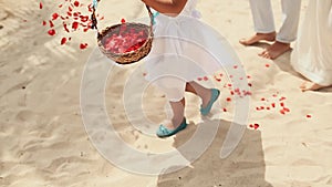 A little girl throws petals of red roses at the feet of the newlyweds. Wedding on the tropical coast. Philippines.