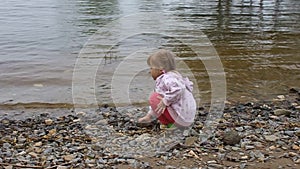 The little girl throws stones into the river ashore