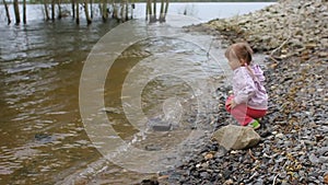 The little girl throws stones into the river ashore