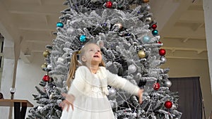 Little girl tosses gift box up. Christmas mood and tree behind child