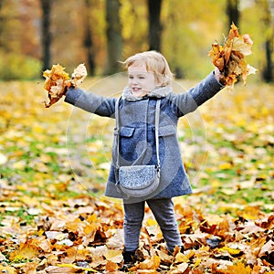 Little girl tossing leaves in autumn park