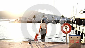 Little girl touches the rope at the mooring bollard on the pier, holding her mother hand