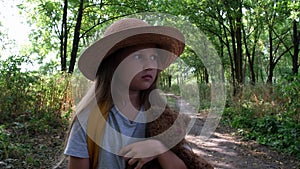 Little girl tourist in a hat with backpack and teddy bear walks alone in the woods. Child lost in the forest. Upset kid