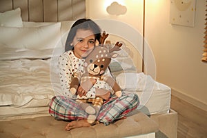 Little girl with toy deer in bedroom lit by lamp