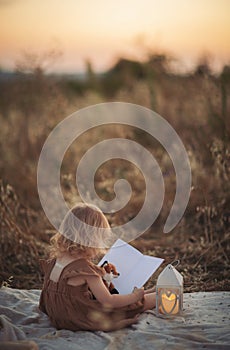 Little Girl with toy reading the book on rural landscape, toned image.