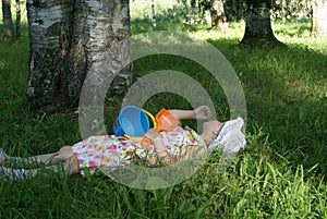 Little girl with toys lying on the grass in the forest