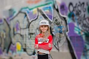 Little girl in a tracksuit dancing modern dance in the street in the background color of the wall. Young urban hip hop dancer