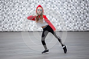 Little girl in a tracksuit is dancing modern dance on the street. Young urban hip hop dancer