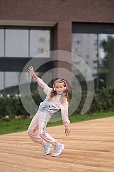 Little girl in a tracksuit is dancing modern dance on the street. Young urban hip hop dancer