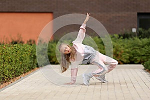 Little girl in a tracksuit is dancing modern dance on the street. Young urban hip hop dancer