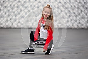 Little girl in a tracksuit is dancing modern dance on the street. Young urban hip hop dancer