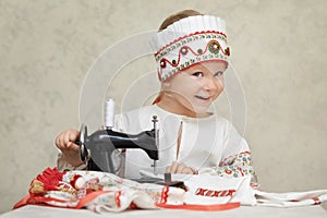 Little girl in the traditional russian shirt and kokoshnik at the process of sewing