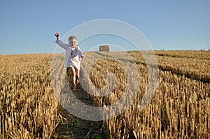 A little girl in a traditional slavic ornamented Ñhemise running barefoot in a harvested field