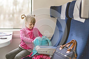 Little girl travel by train. Kid sitting in comfortable chair and looking in backpack. Things to take with on railroad trip with