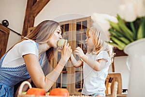 Little girl treats her mother to an apple at the kitchen