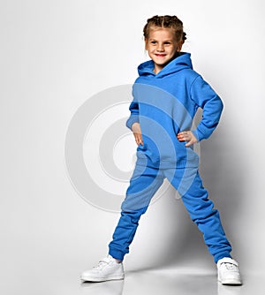 little girl in a trendy blue tracksuit having fun on a white background. A child with an emotional expression stands