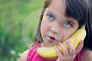 Little girl tries to speak by means of a banana instead of phone