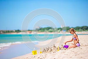 Little girl at tropical white beach making sand castle